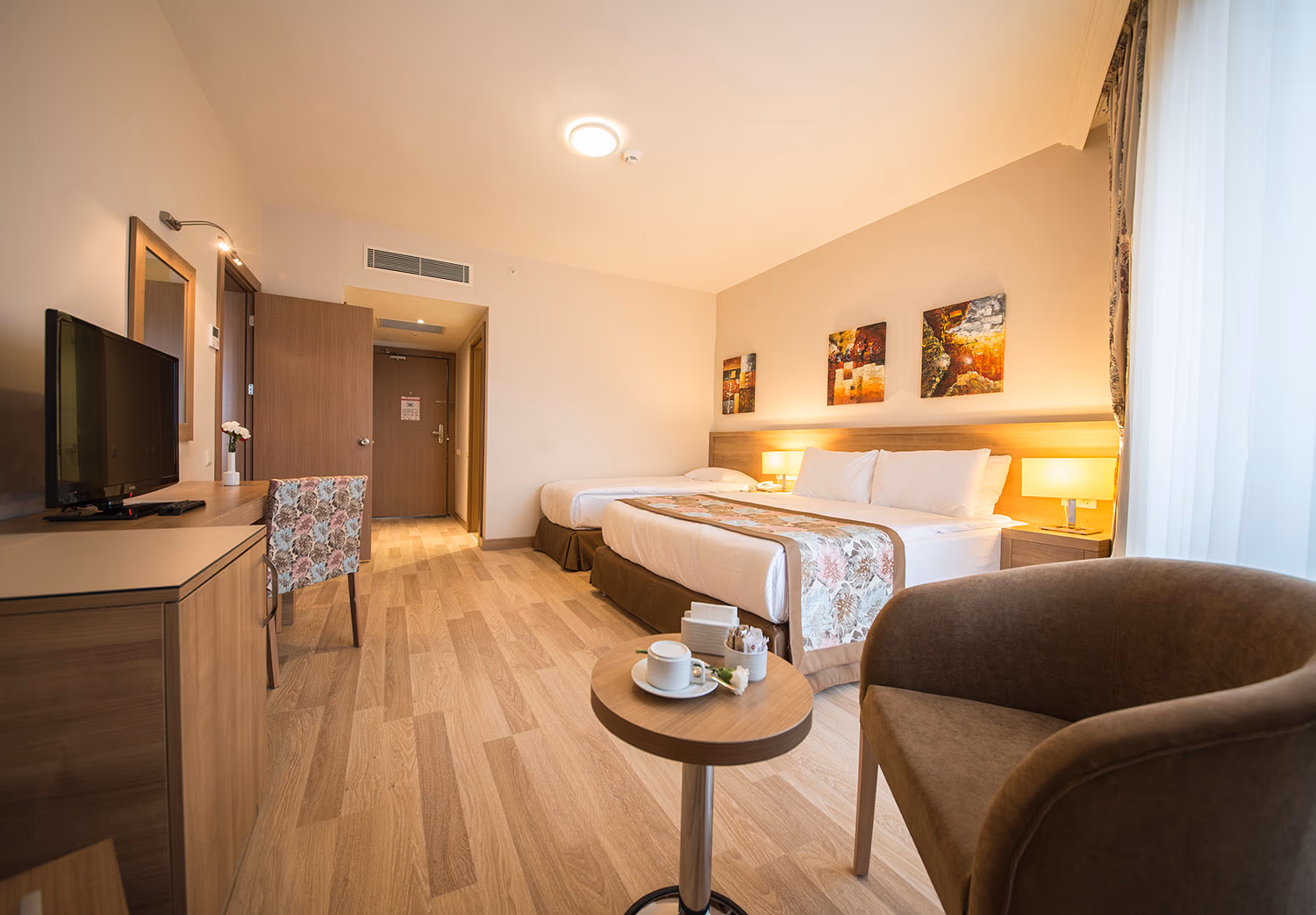 Kamer met een tweepersoonsbed, een eenpersoonsbed, een televisie, een fauteuil en een groot raam bij Wyndham Garden Lara in Lara bij Antalya
