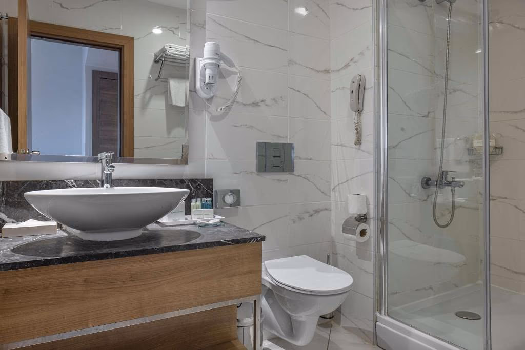 Badkamer met een douchecabine, een wastafel op een houten kast en marmerlook-tegels bij Wyndham Garden Lara in Lara bij Antalya